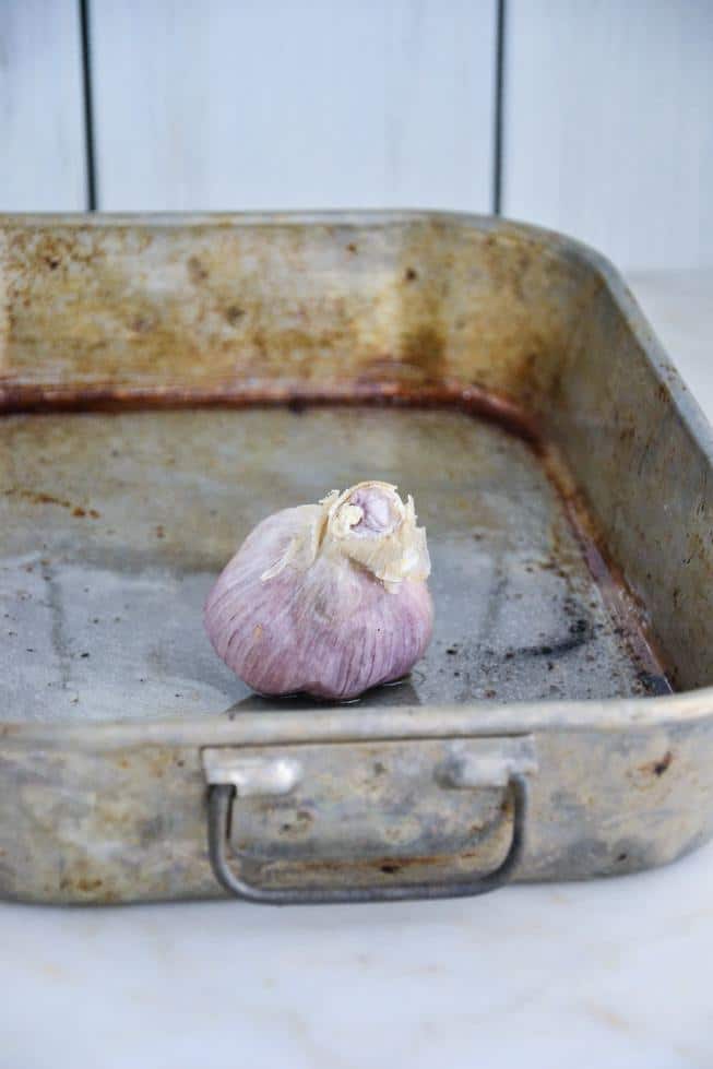 A head of garlic in a large roasting pan ready to be roasted.