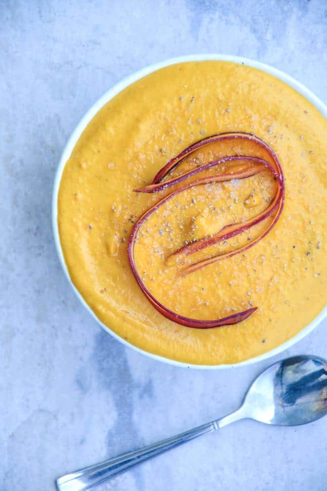 Looking down on a full bowl of orange, creamy carrot sweet potato soup, topped with a sliver of carrot.