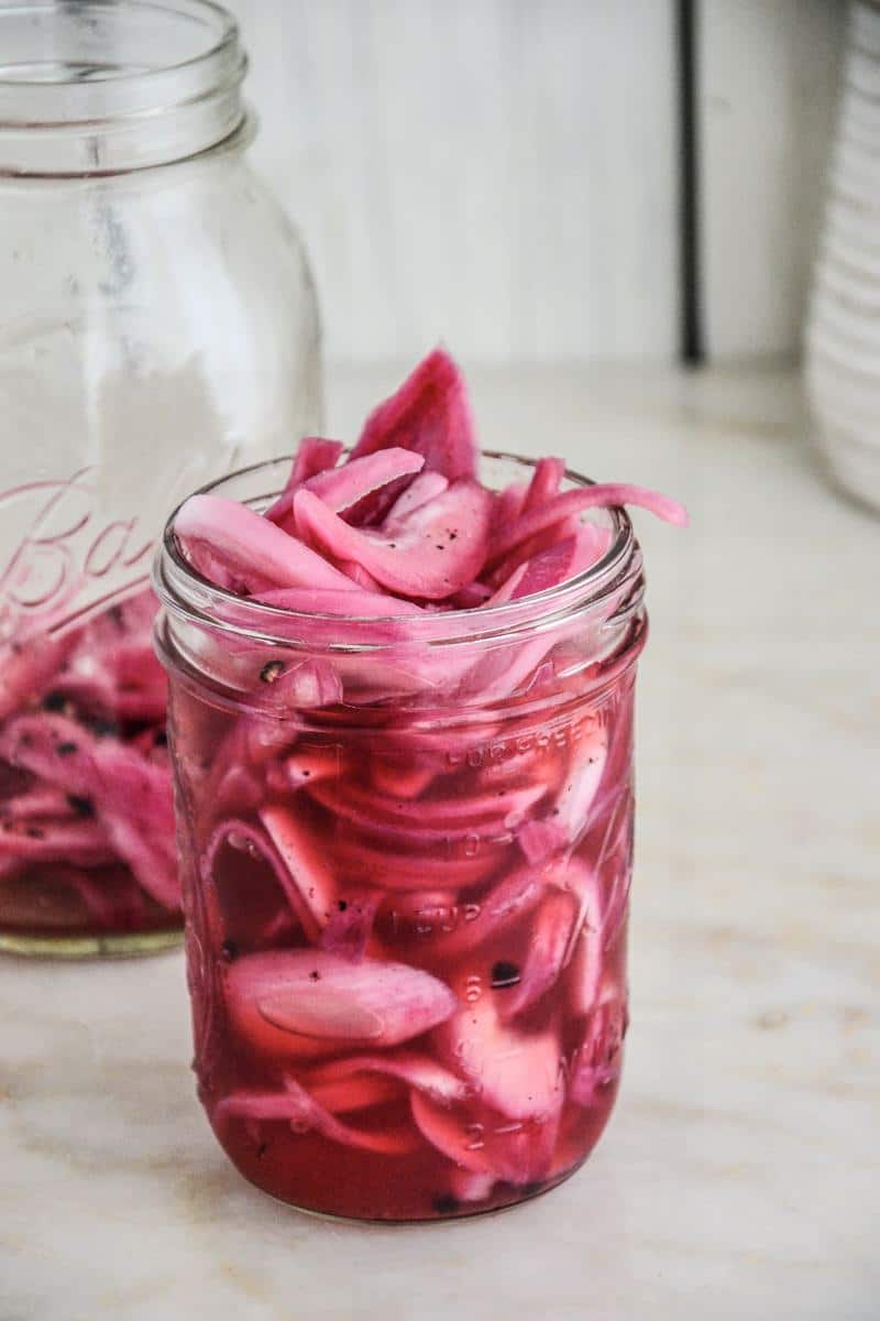 A small mason jar overflowing with bright pink pickled onions, sitting on top of a counter.